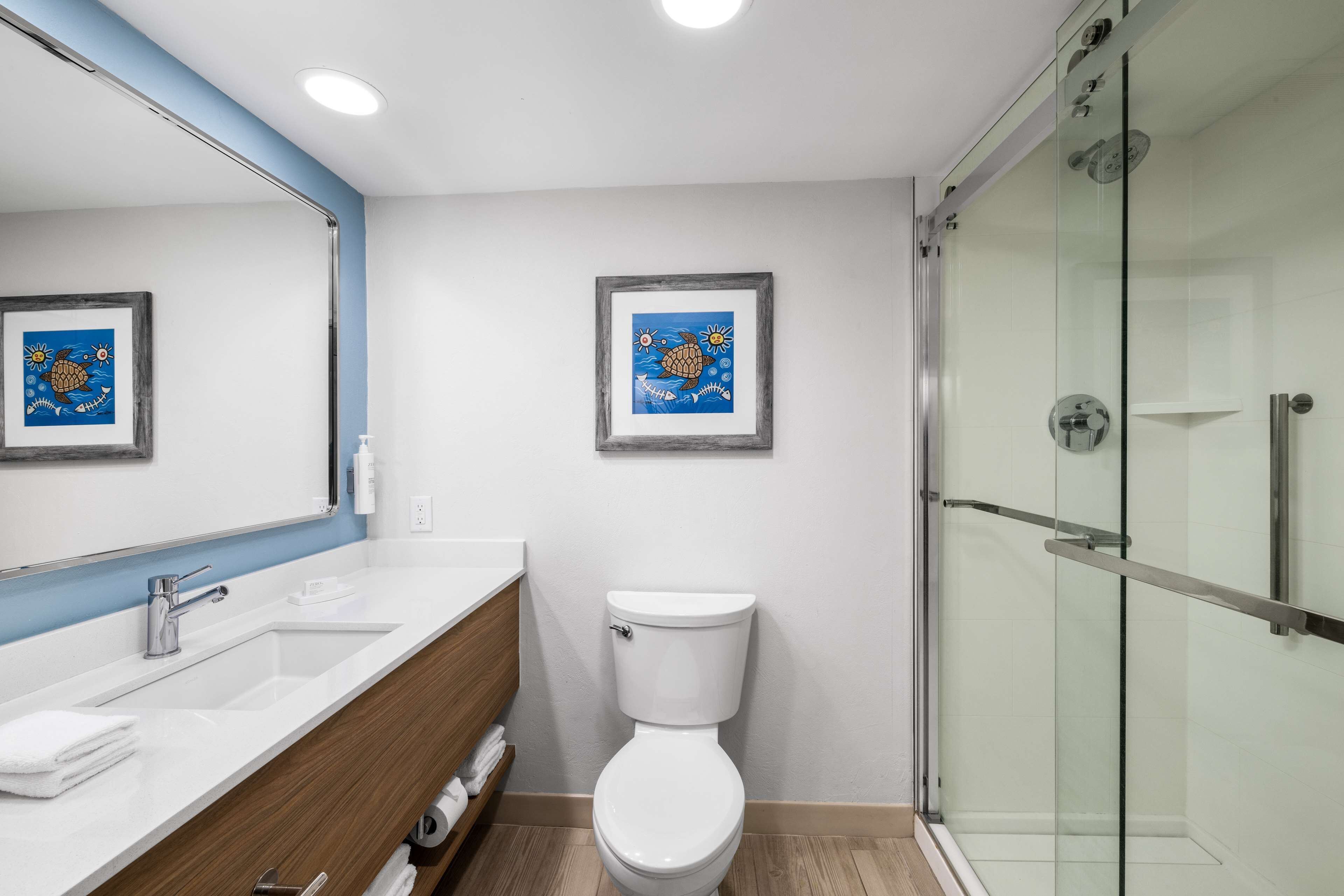 Un baño moderno con un lavabo blanco, tocador de madera, inodoro blanco y cabina de ducha con paredes de vidrio.