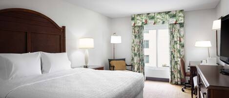 A hotel room with a large bed, two bedside tables with lamps, a desk with a television, and a window with curtains.