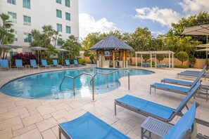 A pool area with lounge chairs, a gazebo, and a building in the background. - Hampton Inn & Suites San Juan (Carolina)