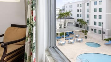 A hotel room with a view of a pool area, outdoor seating, and a building with multiple floors.