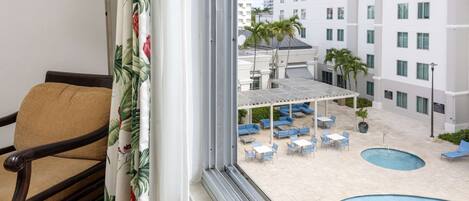Habitación de hotel con vistas a una zona de piscina, mobiliario exterior y un edificio de varios pisos.