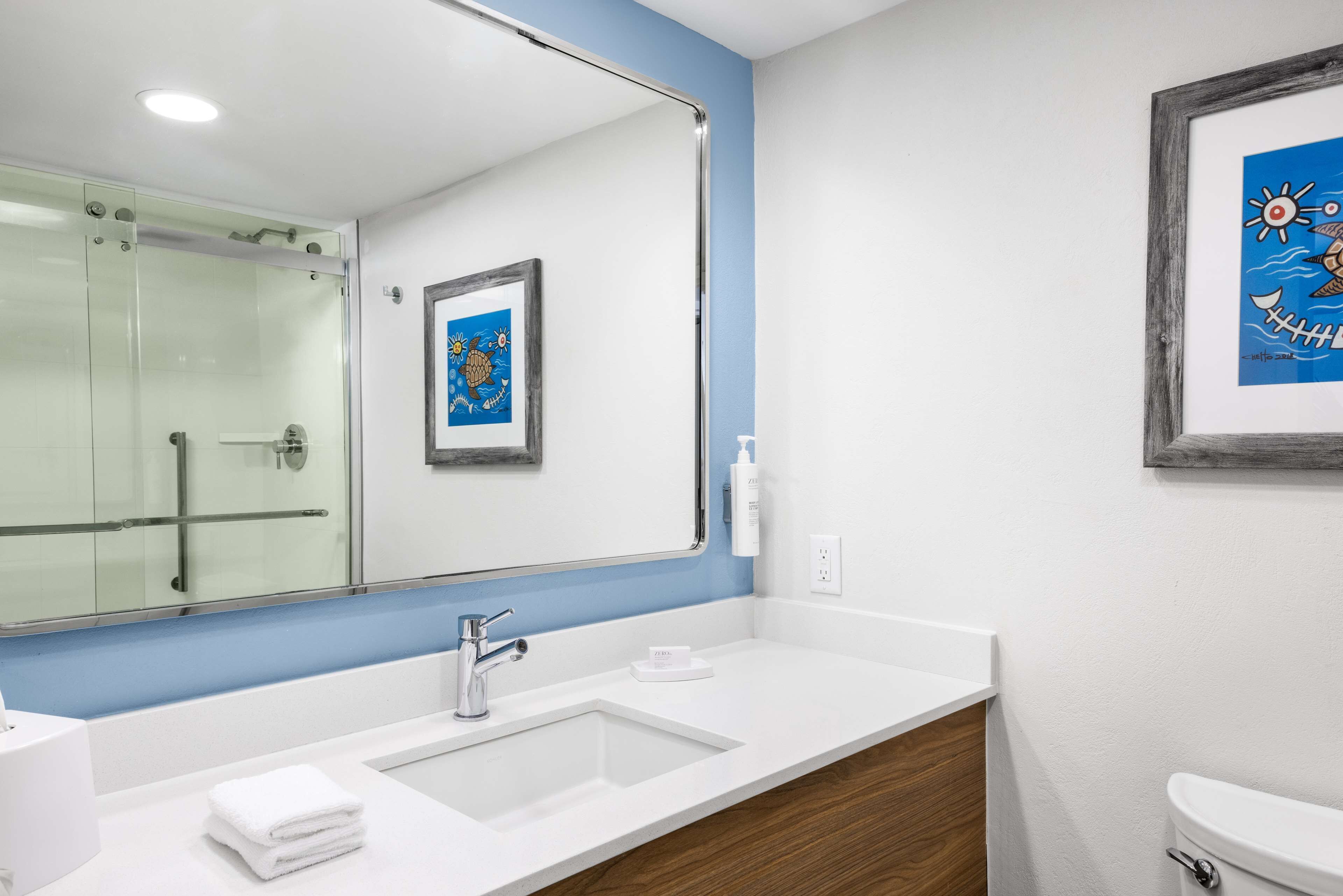 A modern bathroom with a large mirror, a white sink, and a glass shower enclosure.