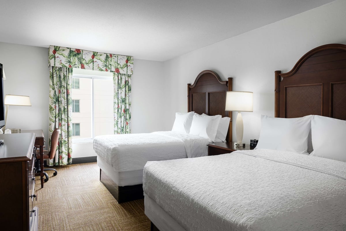 A hotel room with two beds, a desk, a chair, and a window with curtains.