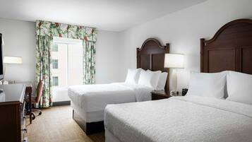 Habitación de hotel con dos camas, un escritorio, una silla y una ventana con cortinas.