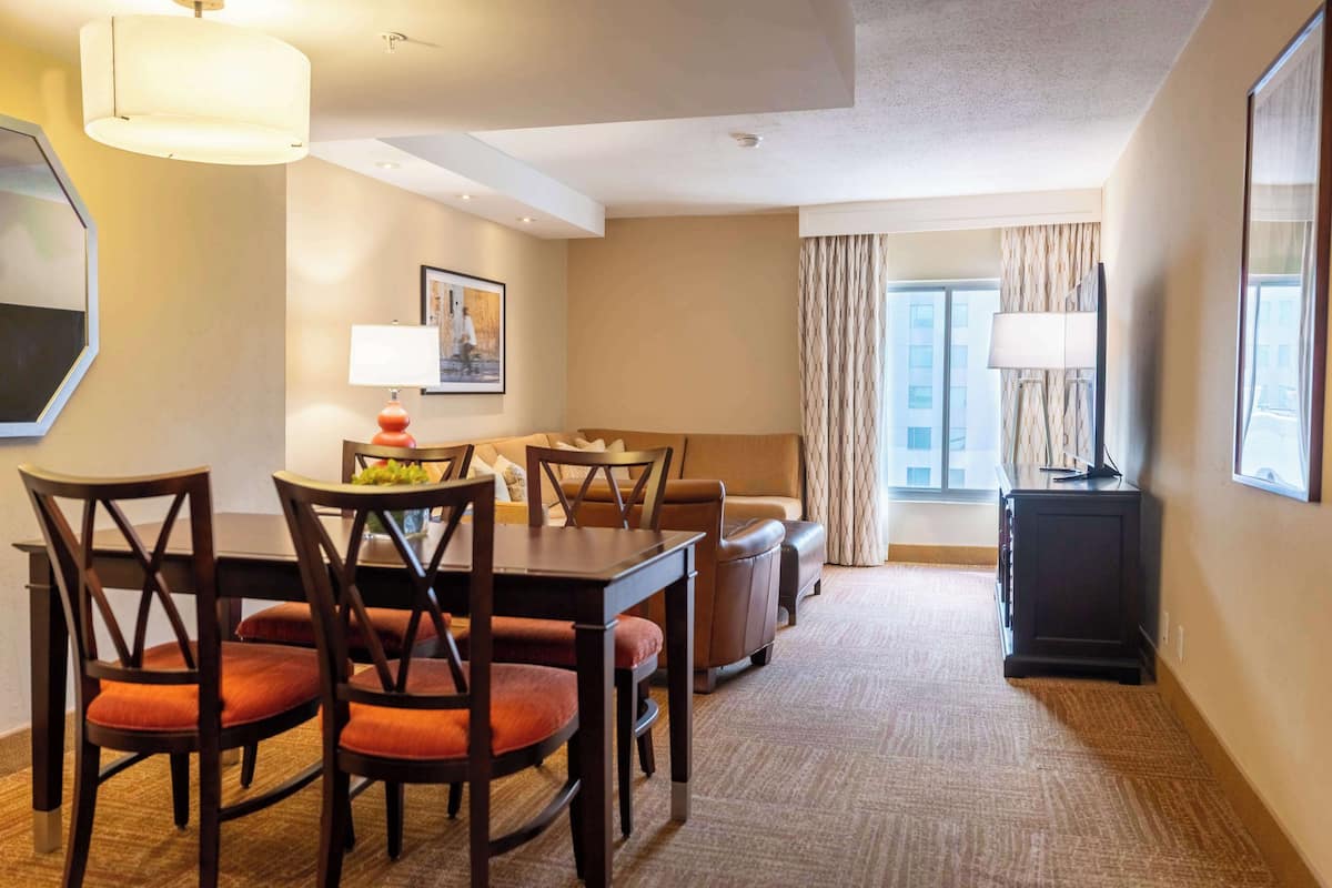 A hotel room with a dining area, a sofa, a TV, and a window with curtains.
