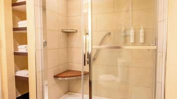 Ducha con cerramiento de vidrio, estante de madera, puerta de vidrio y un estante con artículos de tocador.