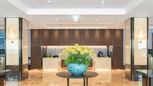 A modern lobby with a reception desk, a decorative blue vase with flowers, and a patterned wall. - Jeju Sun Hotel & Casino (Jeju City)