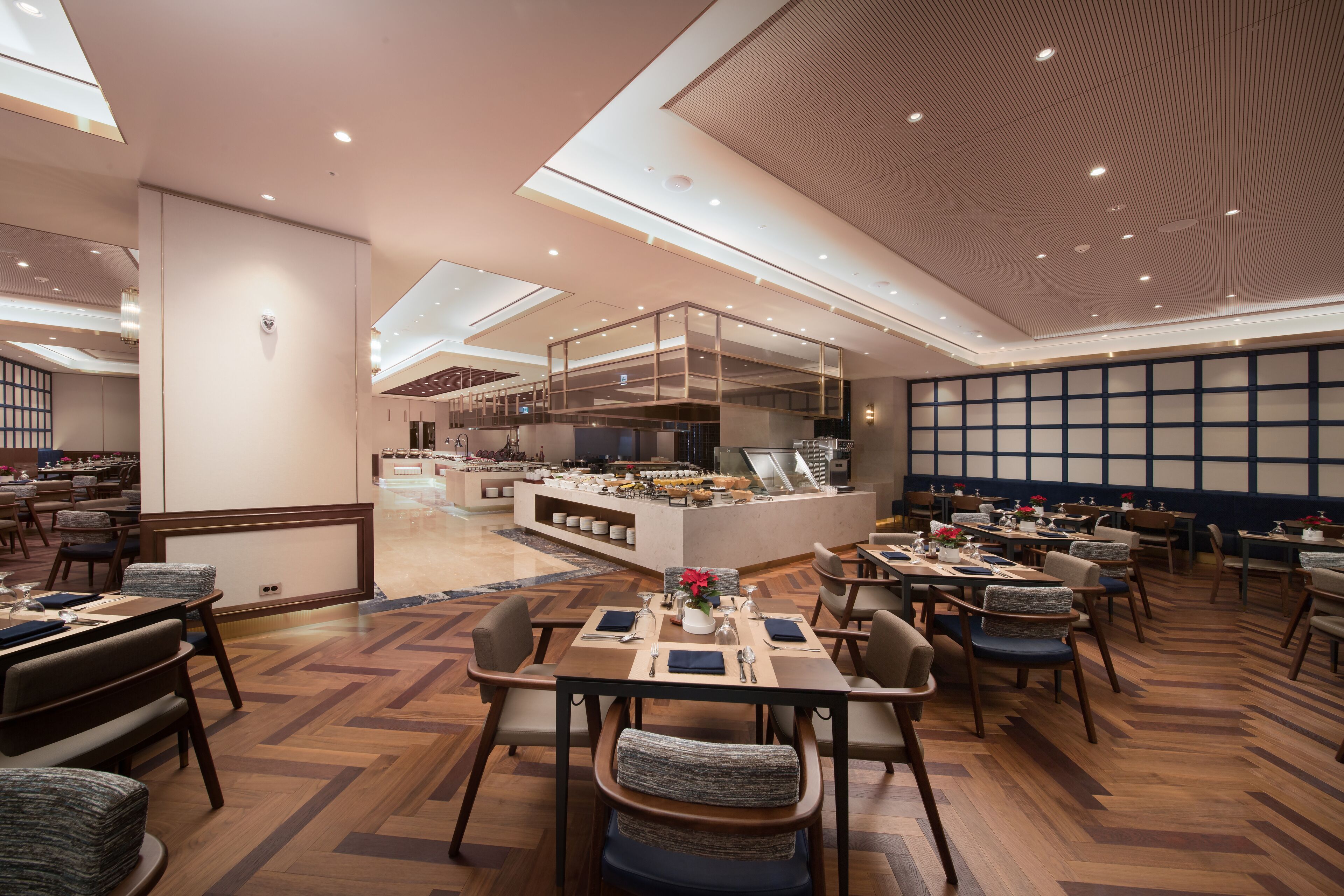 Um restaurante espaçoso com pé direito alto, iluminação moderna e uma ilha central com cozinha.