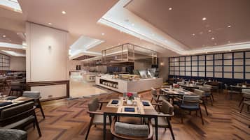 Um restaurante espaçoso com pé direito alto, iluminação moderna e uma ilha central com cozinha.