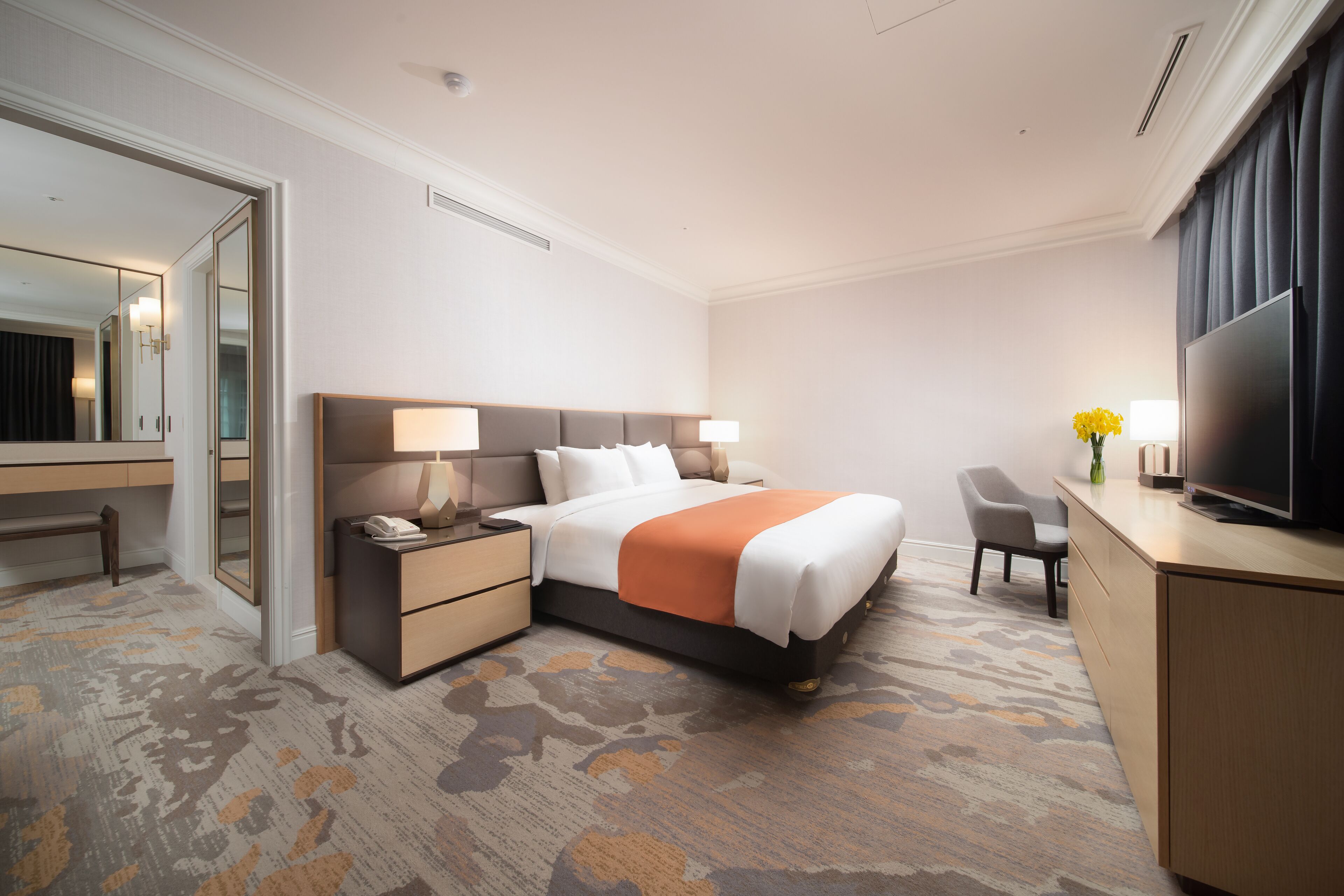 A hotel room with a large bed, bedside tables, a desk with a TV, a chair, and a mirror.