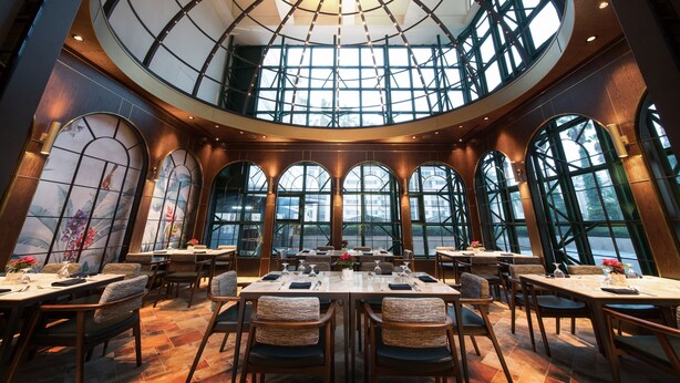 A spacious dining area with high ceilings, large windows, and a central skylight. Tables are set with chairs, and the room has a modern architectural design. - Jeju Sun Hotel & Casino (Jeju City)
