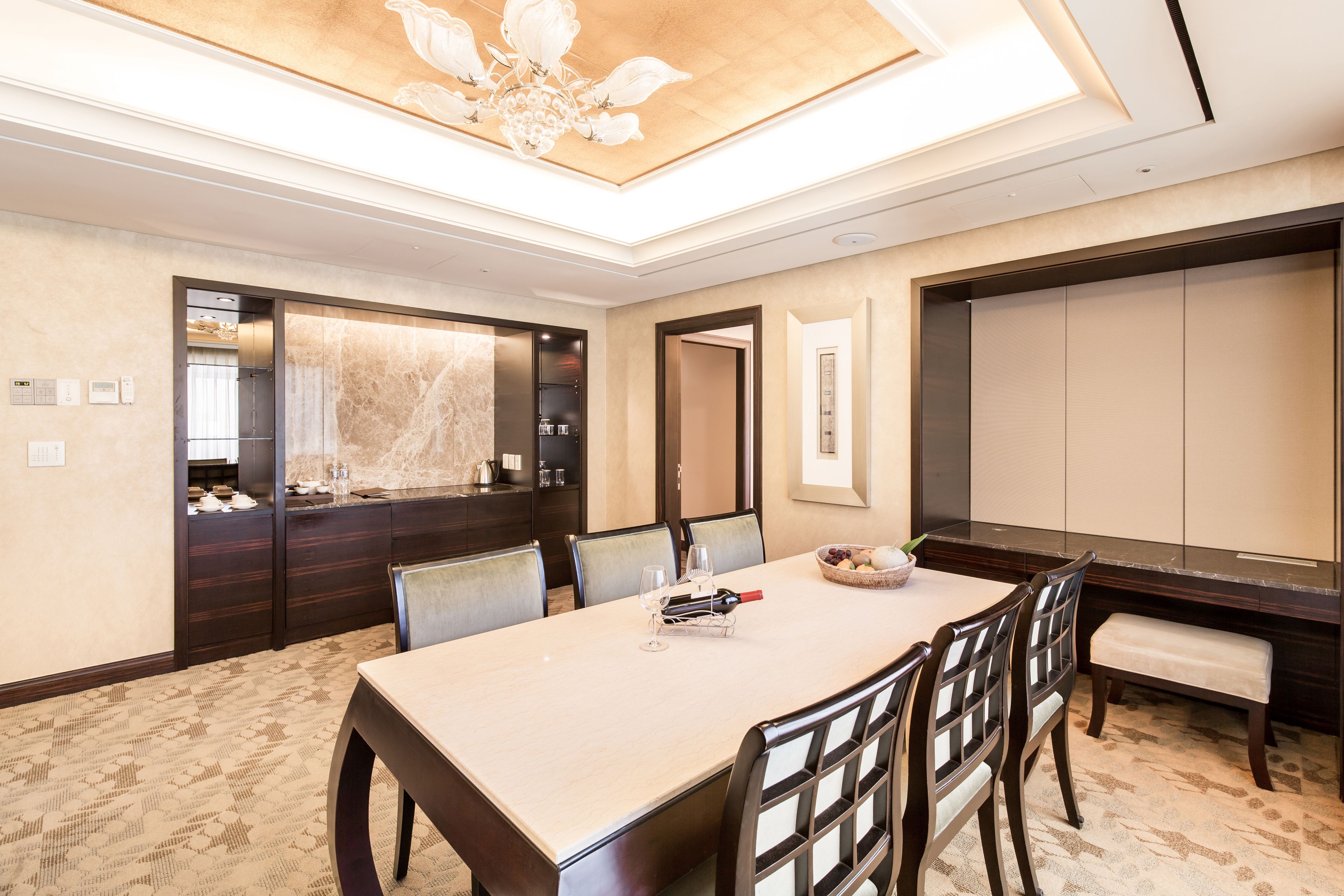 A modern hotel dining room with a large table, chairs, a chandelier, and a large mirror.