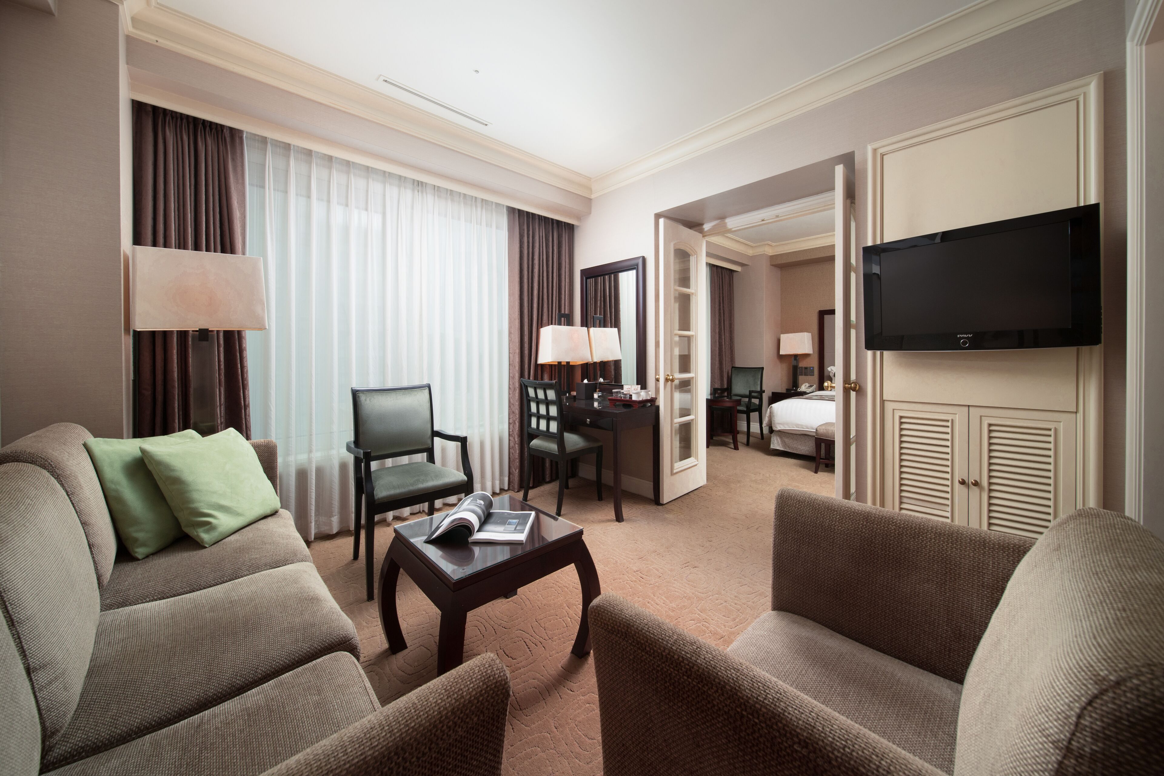 Ein Hotelzimmer mit Sofa, Sesseln, einem Couchtisch, einem Fernseher, einem Schreibtisch und einem Kleiderschrank.