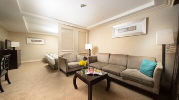 Un salón con alfombra color beige, un sofá marrón, un sillón marrón, una mesa de centro de madera con un libro y flores, y un televisor sobre un mueble.