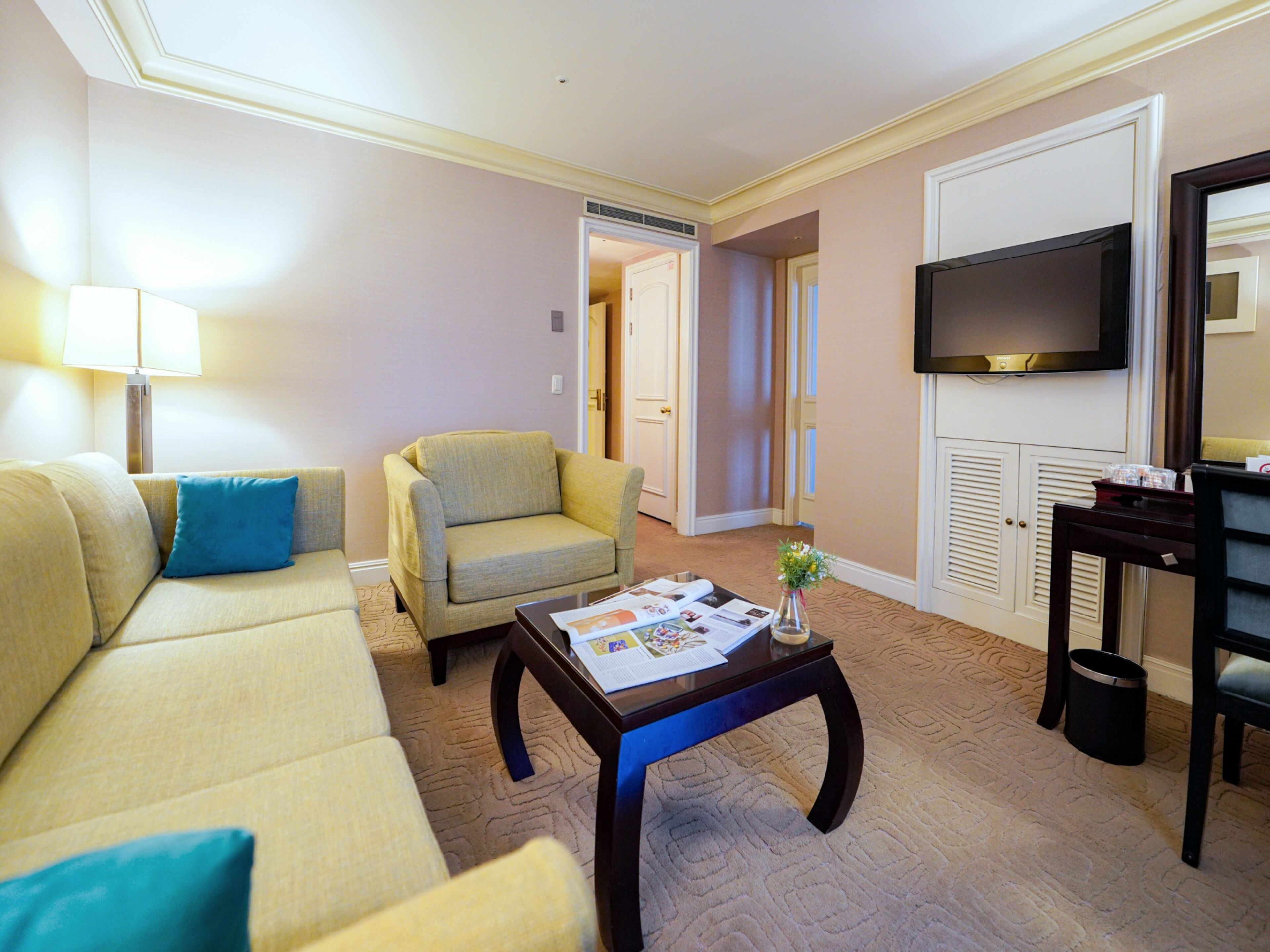 A living room with a sofa, armchair, coffee table, lamp, TV, and a door leading to another room.