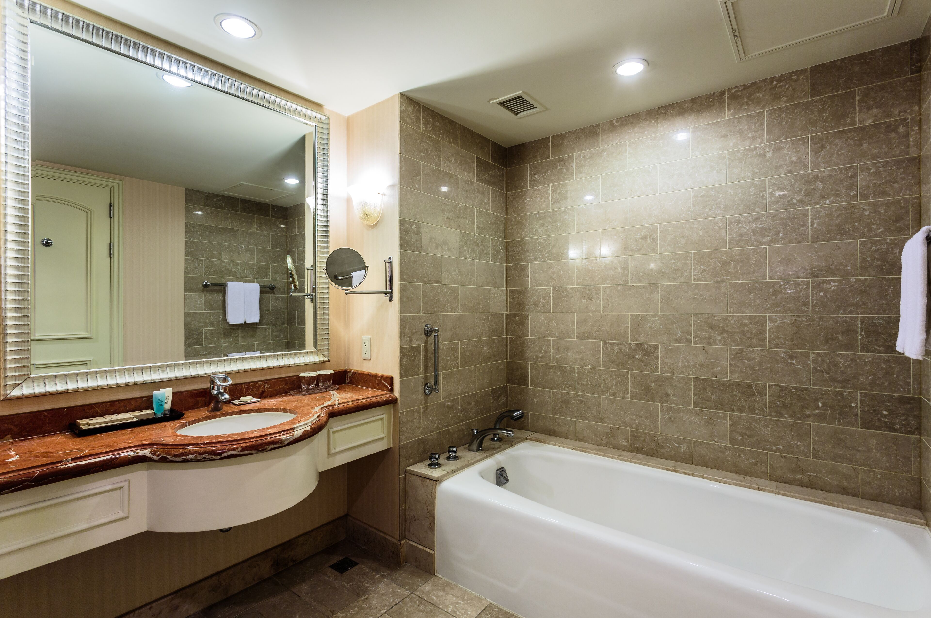 Un baño moderno con un espejo grande, un lavamanos, una bañera y un tocador con un perchero para toallas.