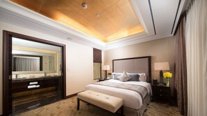 A hotel room with a large bed, a bench, a mirror, a nightstand, and a bathroom with a vanity. - Jeju Sun Hotel & Casino (Jeju City)