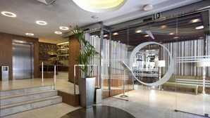 A modern hotel lobby with a staircase, a reception desk, and a large potted plant. - Hotel Ópera (Madrid)
