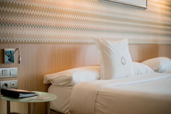 A hotel room with a bed, a bedside table with a lamp, and a wall with a zigzag pattern.