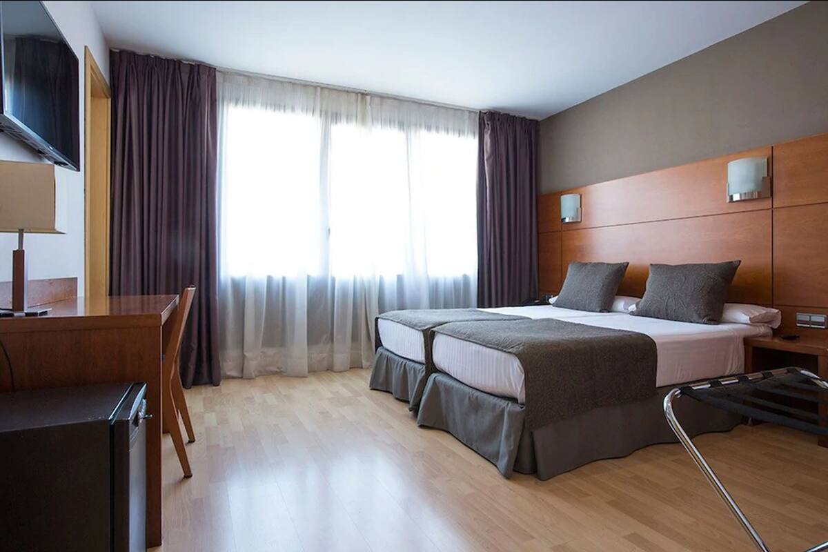 Une chambre d’hôtel avec deux lits, un bureau, une télévision et une fenêtre avec des rideaux.