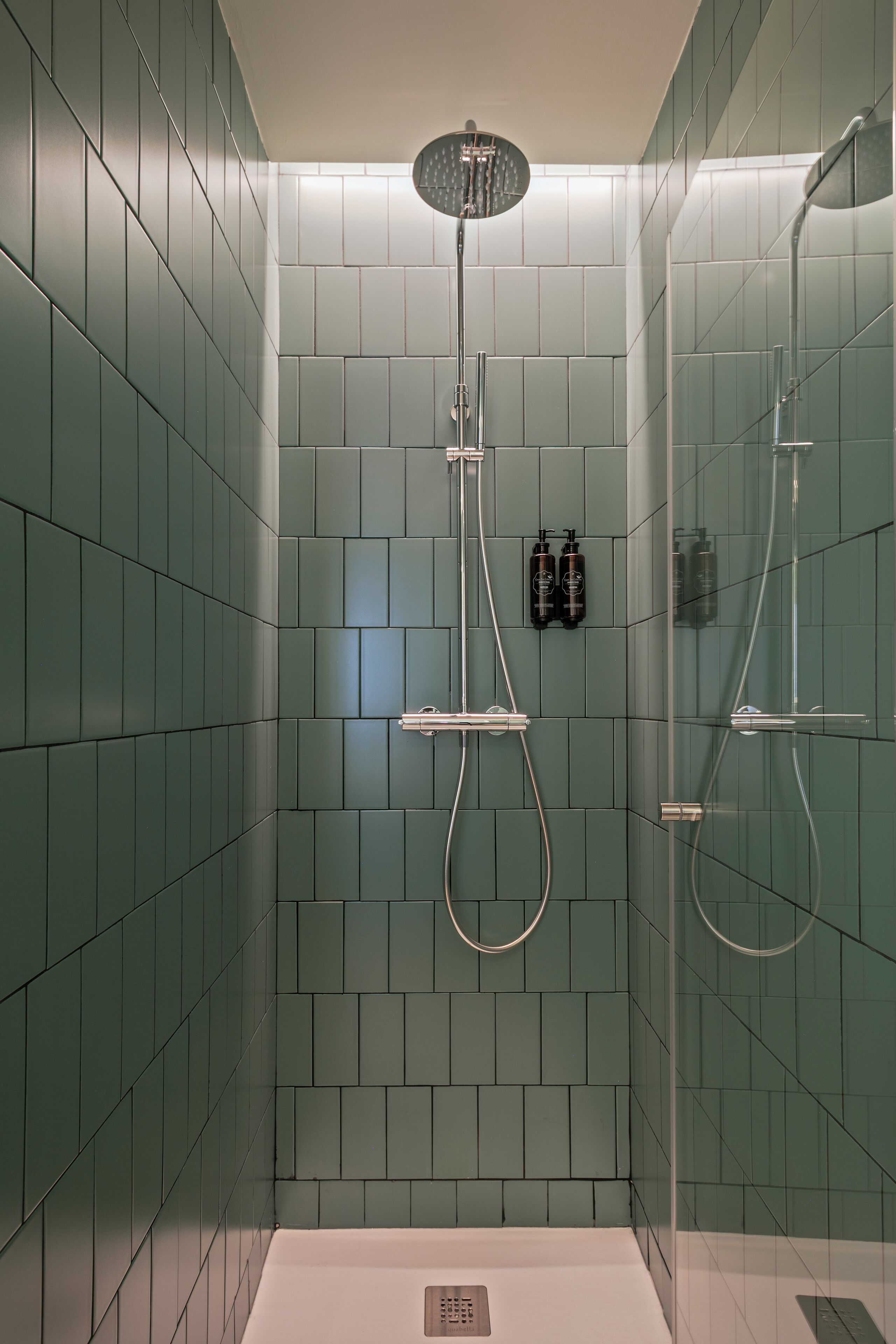Une douche moderne dotée d’une paroi en verre, de carreaux verts et d’un panneau de commande.