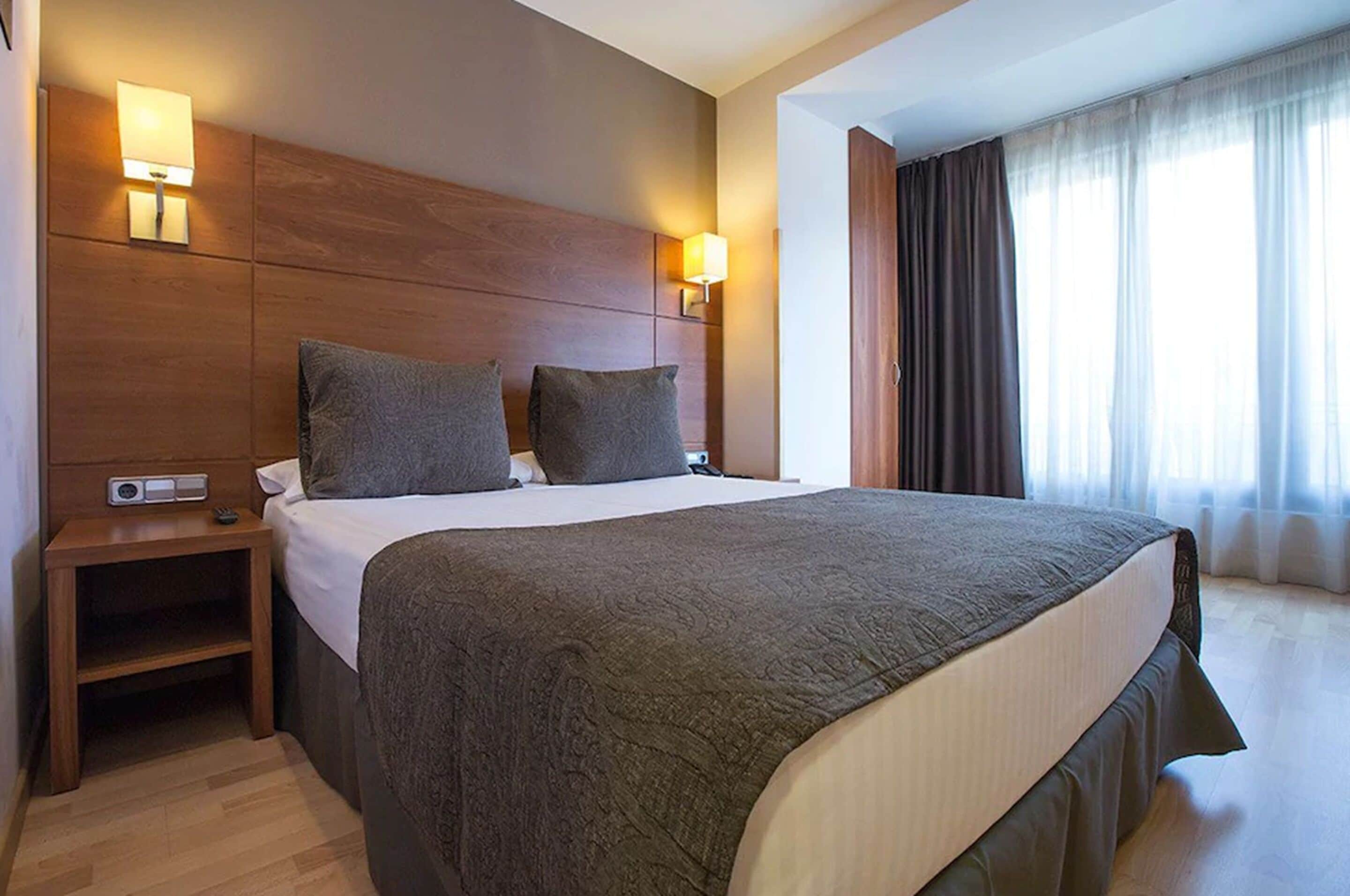 Ein Hotelzimmer mit einem großen Bett, zwei Nachttischlampen, einem Nachttisch und einem fenster mit Vorhängen.