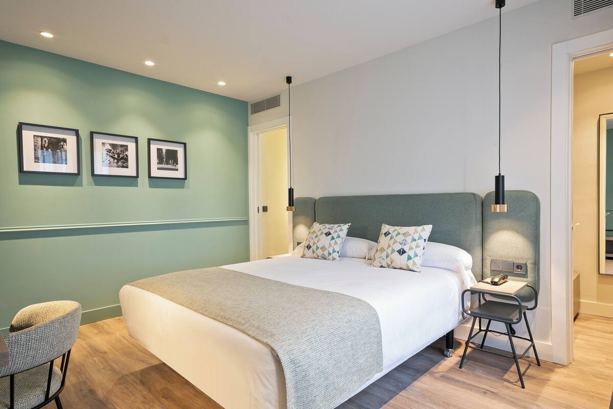 Une chambre moderne avec un grand lit, un bureau et une chaise. Trois tableaux encadrés ornent le mur.