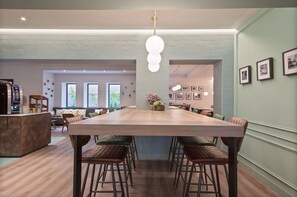A spacious dining area with a long wooden table and multiple chairs, a bar area with stools, and framed pictures on the walls. - Hotel Via Augusta (Barcelona)
