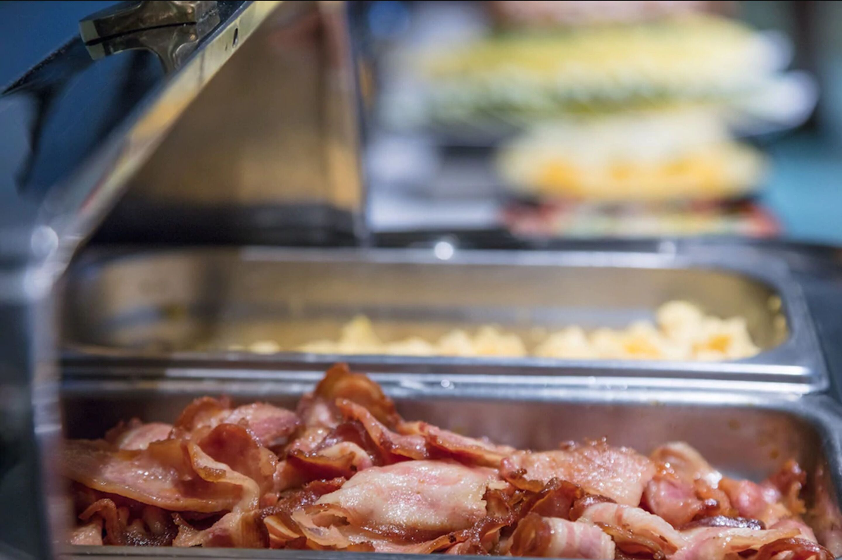A buffet with various food options including bacon and scrambled eggs.