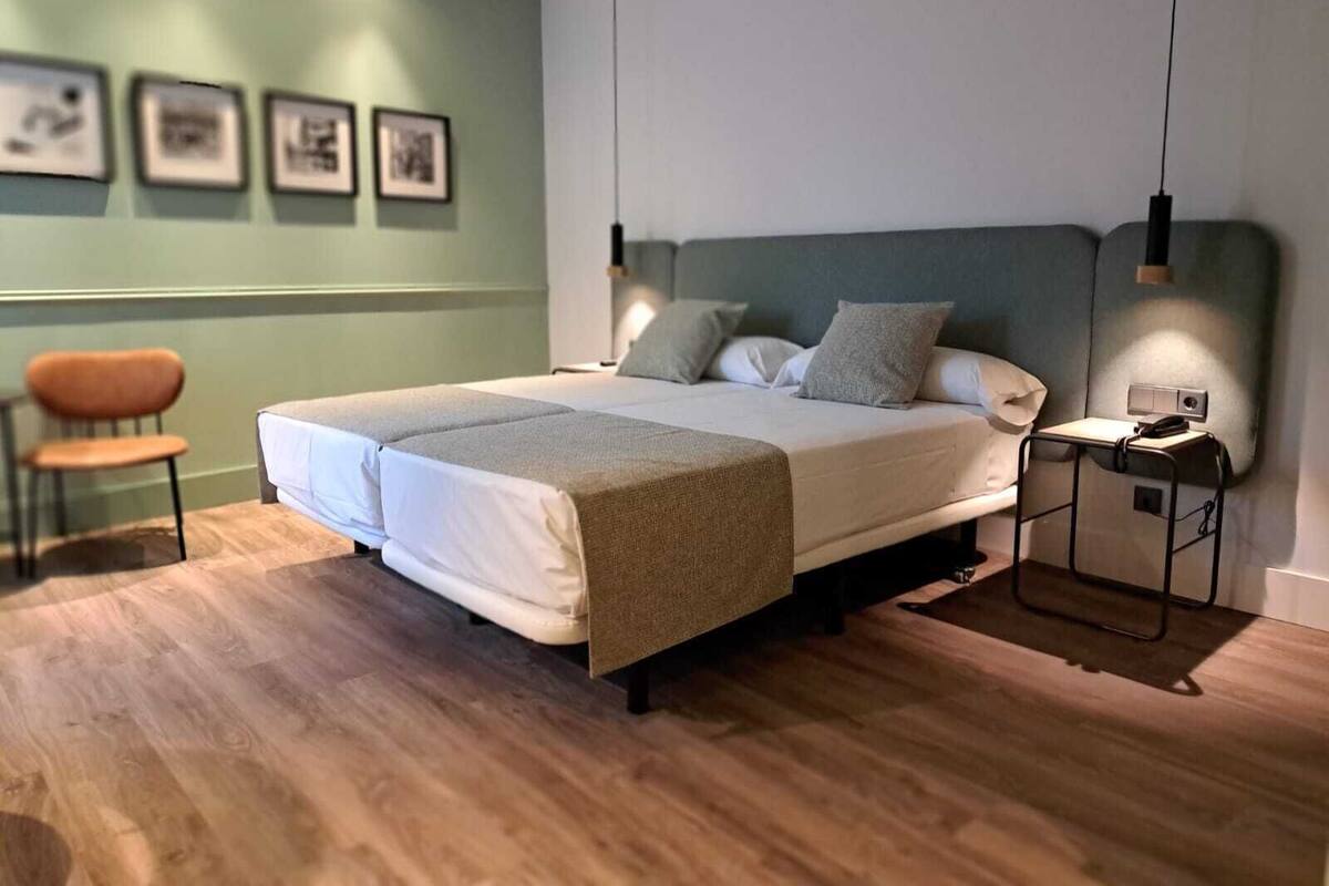 Une chambre à coucher moderne avec un grand lit, une chaise et une table de chevet avec une lampe.