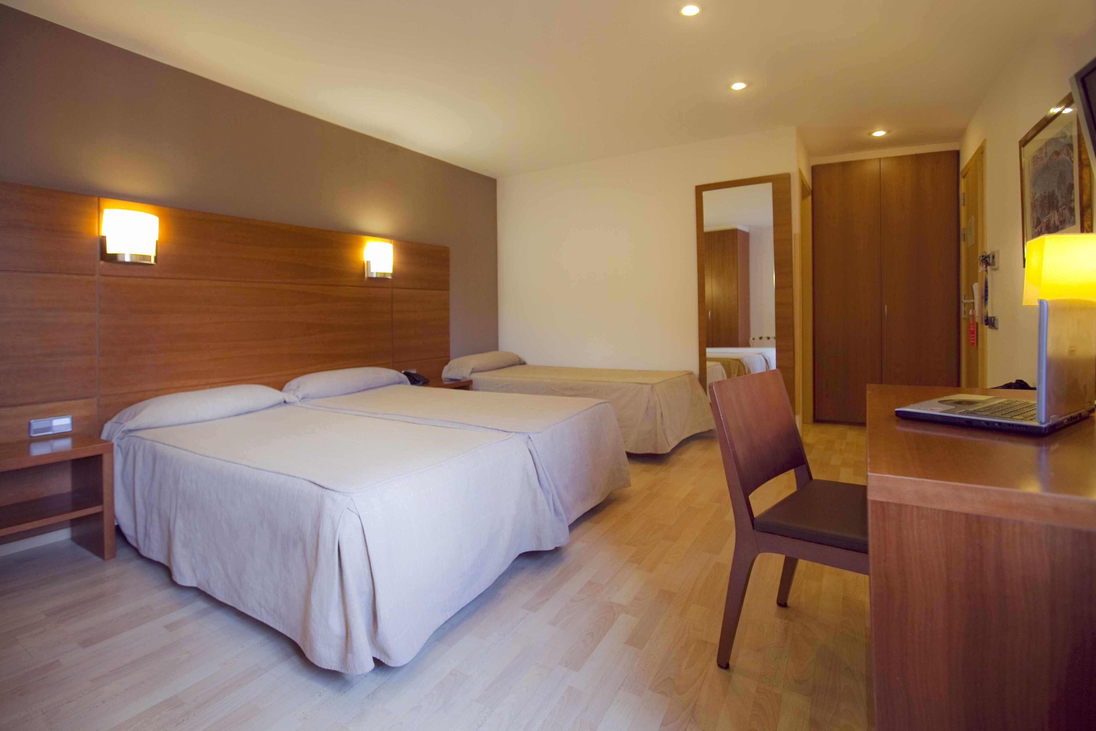 A hotel room with two beds, a desk with a laptop, a chair, and a wooden headboard.