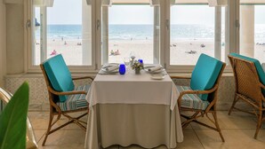 A dining area with a table set for two, overlooking a beach.