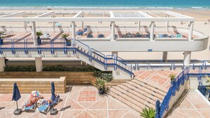 A beachside terrace with sun loungers and umbrellas, a covered seating area, and a view of the beach and ocean.