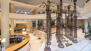 A spacious lobby with a curved reception desk, multiple seating areas, and a high ceiling with decorative lighting fixtures.
