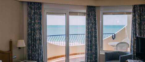 A hotel room with a bed, a desk, a chair, and a balcony with a view of the sea.