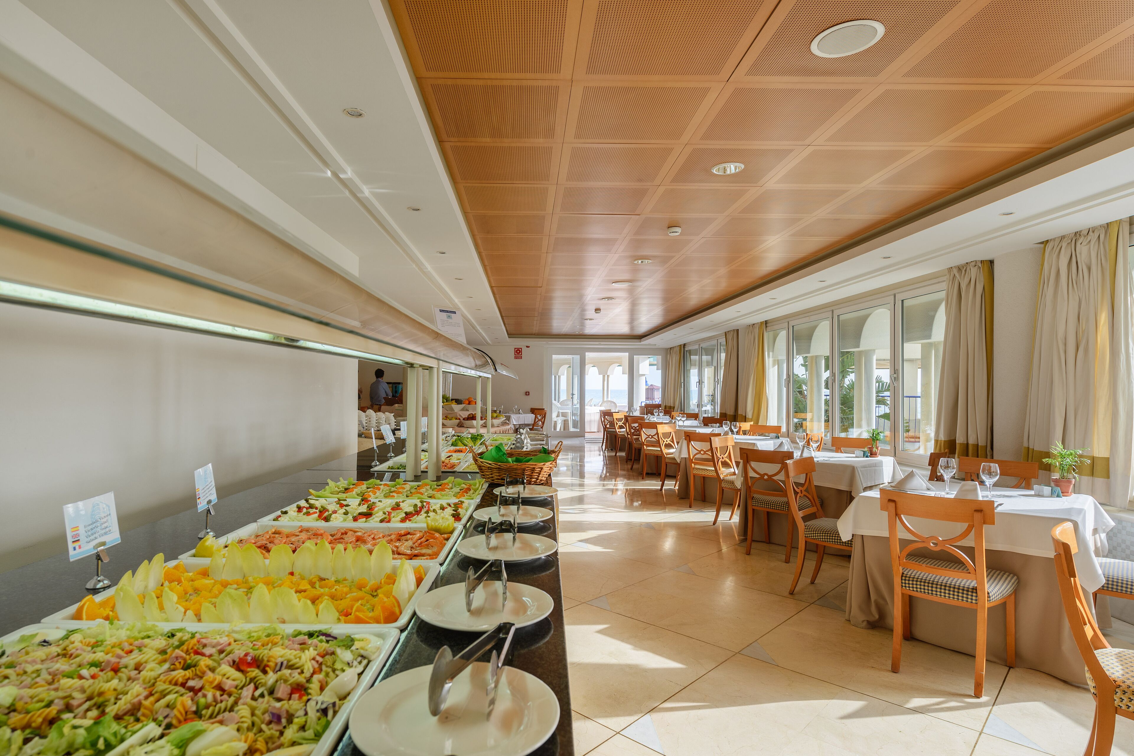 A buffet area with various food options, a seating area with tables and chairs, and large windows allowing natural light.