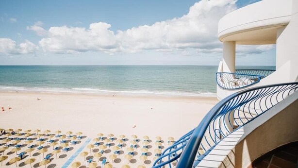 A beach view with a white building, blue chairs, and umbrellas.