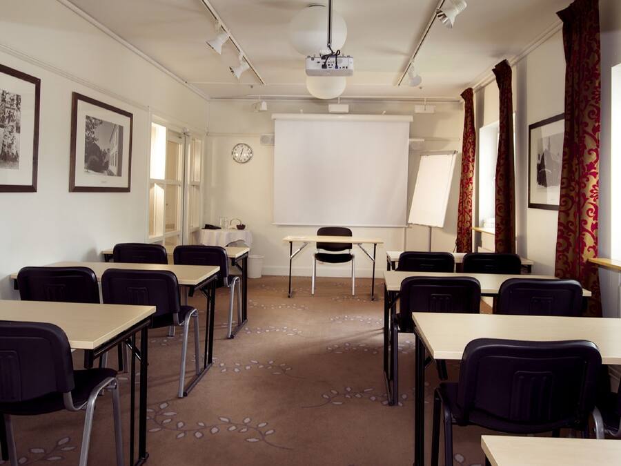 Een vergaderruimte met tafels, stoelen, een beamer, een whiteboard en ingelijste foto's aan de muren.