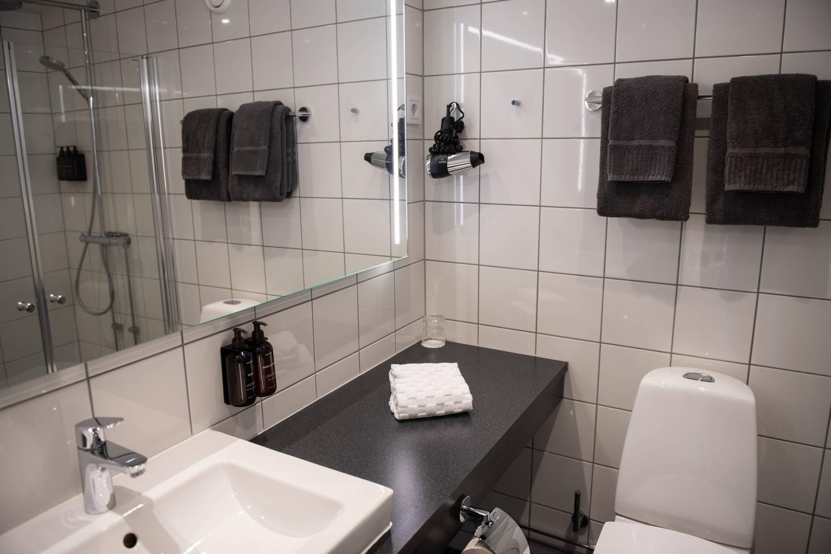 Un baño moderno con cabina de ducha de vidrio, un lavabo blanco, encimera negra y dos toallas colgadas en la pared.