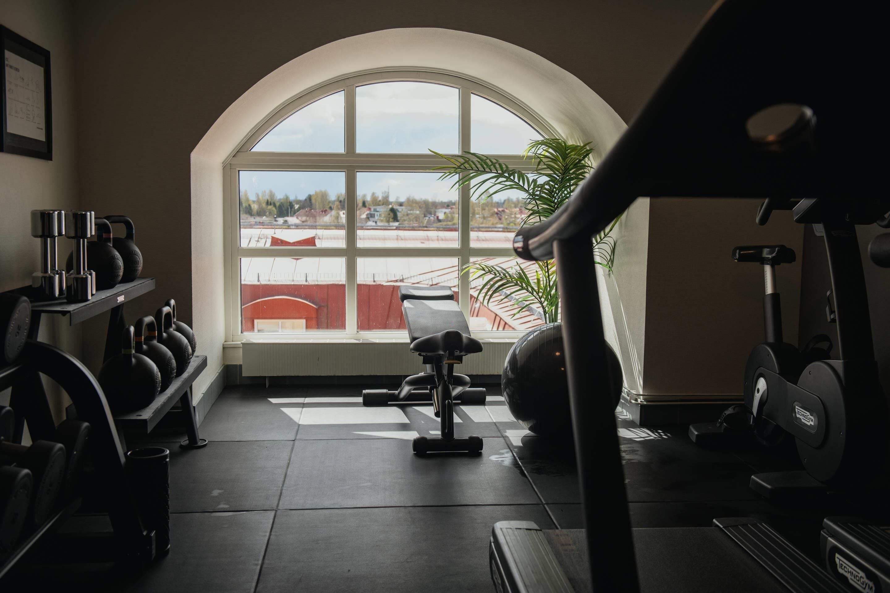 Uma academia com uma grande janela em arco, equipamentos de ginástica e esteira.