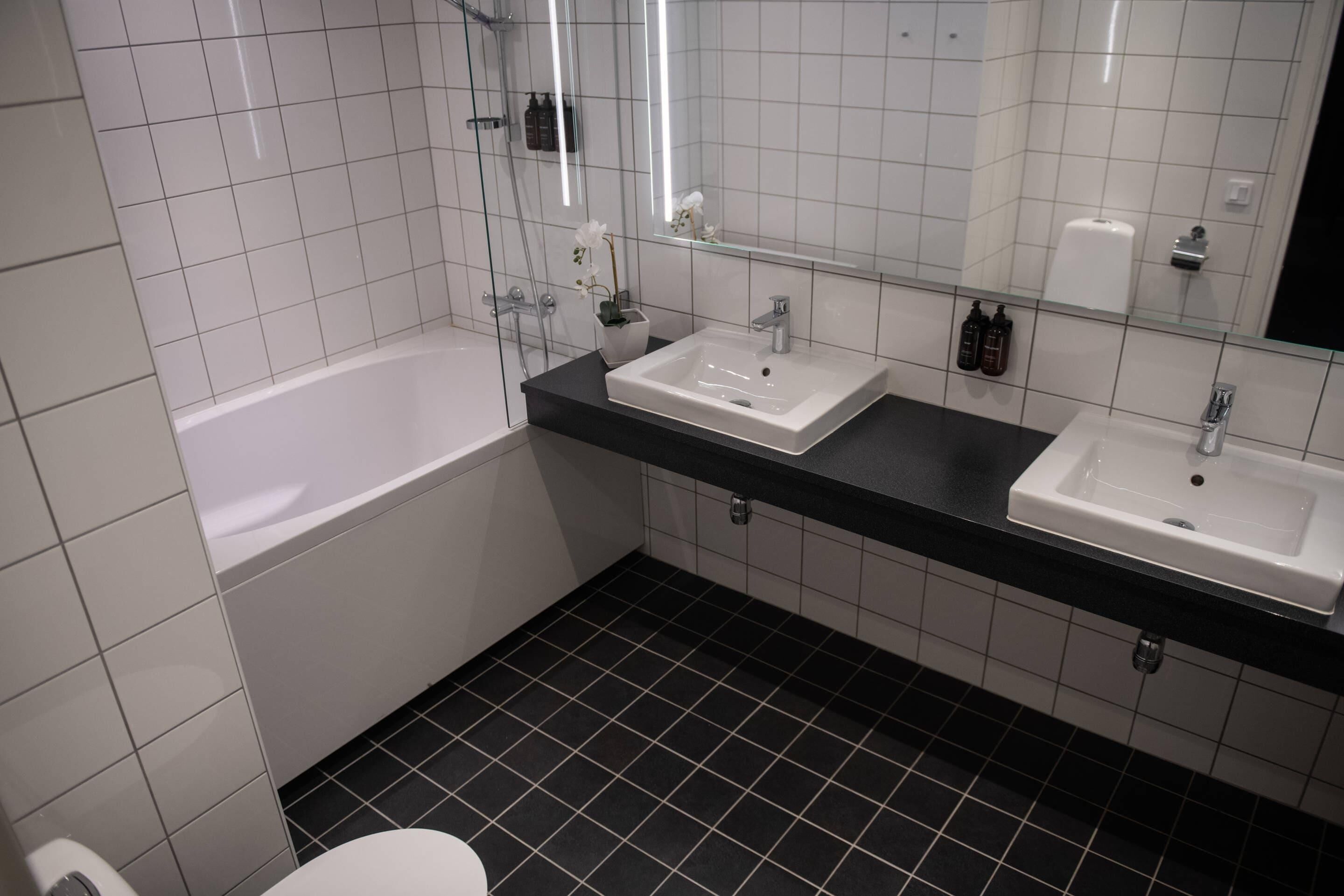 A modern bathroom with two sinks, a bathtub, and a large mirror.