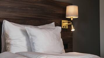 Una cama bien hecha con sábanas blancas, un cabecero de madera y una lámpara fijada a la pared.
