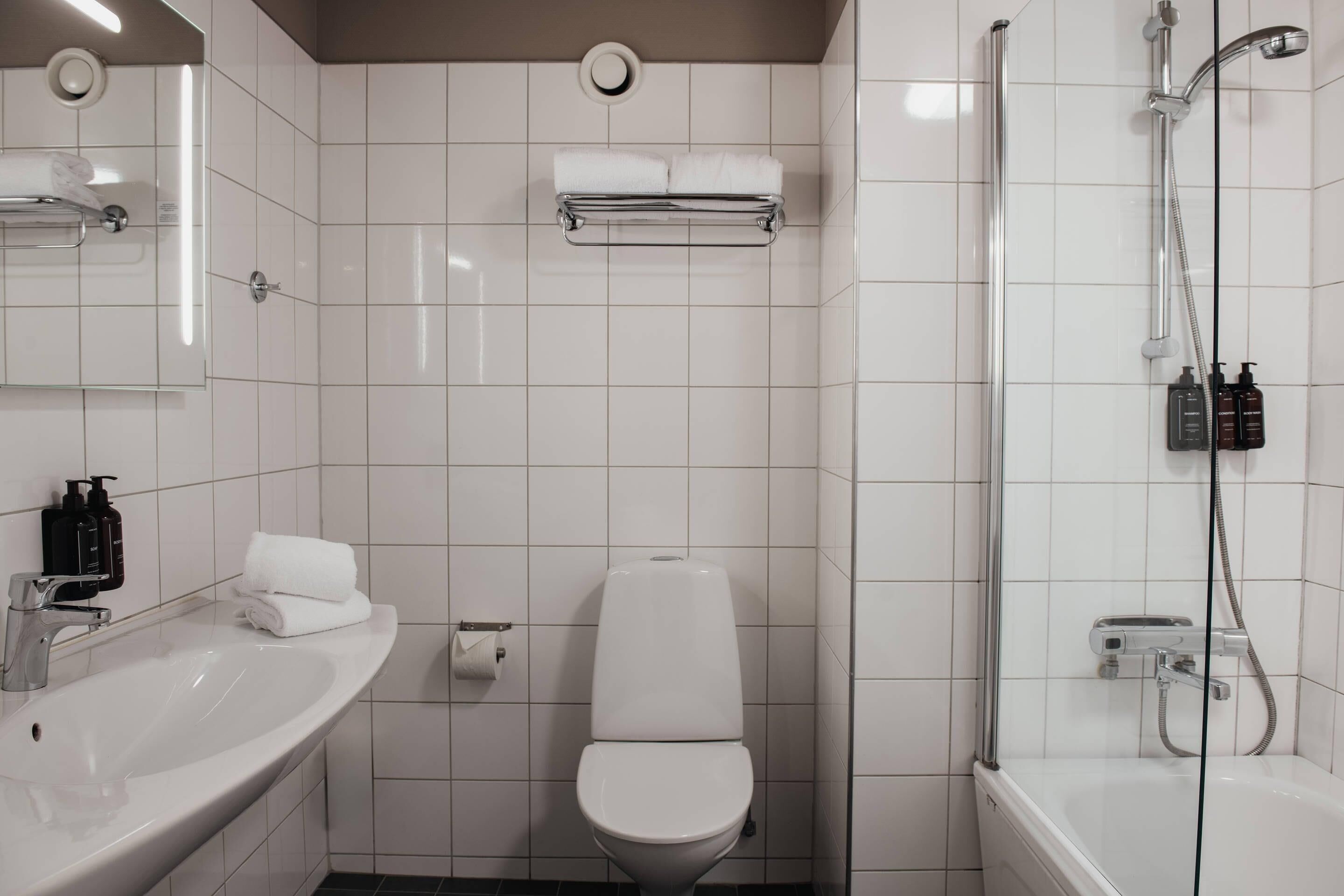 A modern bathroom with a white sink, toilet, and shower. There are two bottles of toiletries on the sink and a towel rack above the toilet.