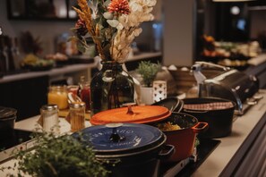 A kitchen counter with various cooking pots and pans, a vase with dried flowers, and kitchen utensils.