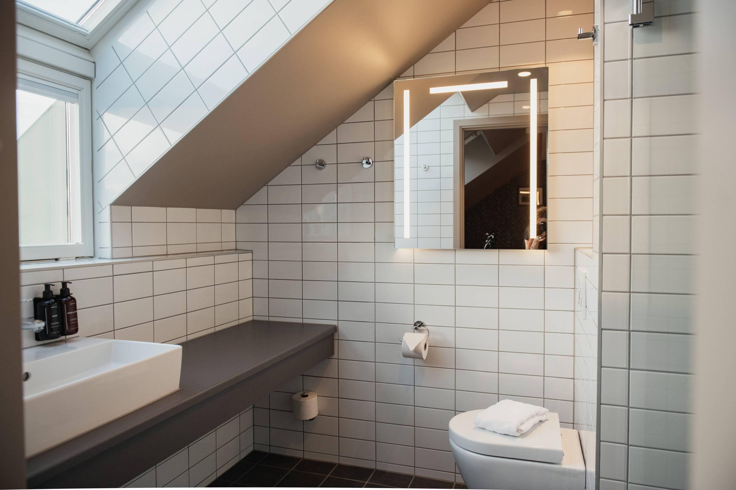 A modern bathroom with a skylight, white tiles, a white sink, and a toilet.