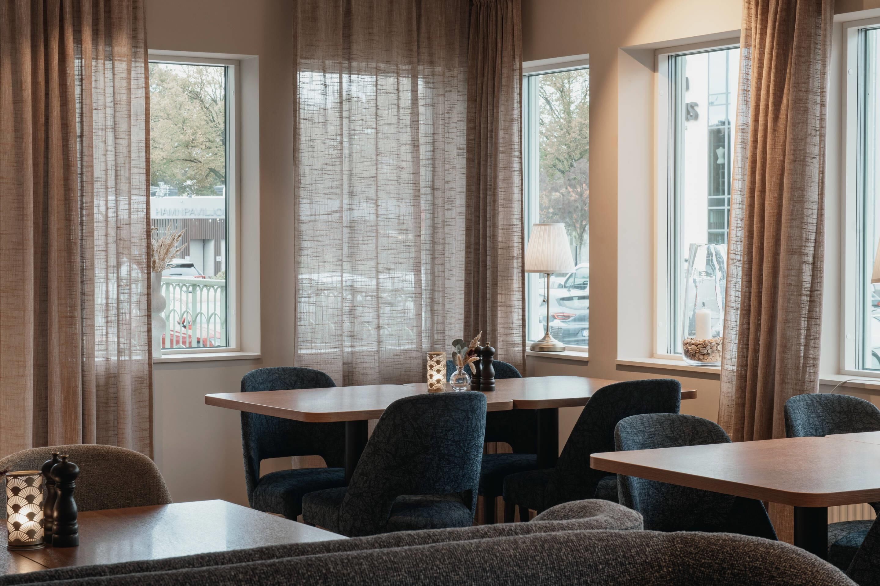 Un comedor con mesa y sillas, ventanas amplias con cortinas y vistas al exterior.