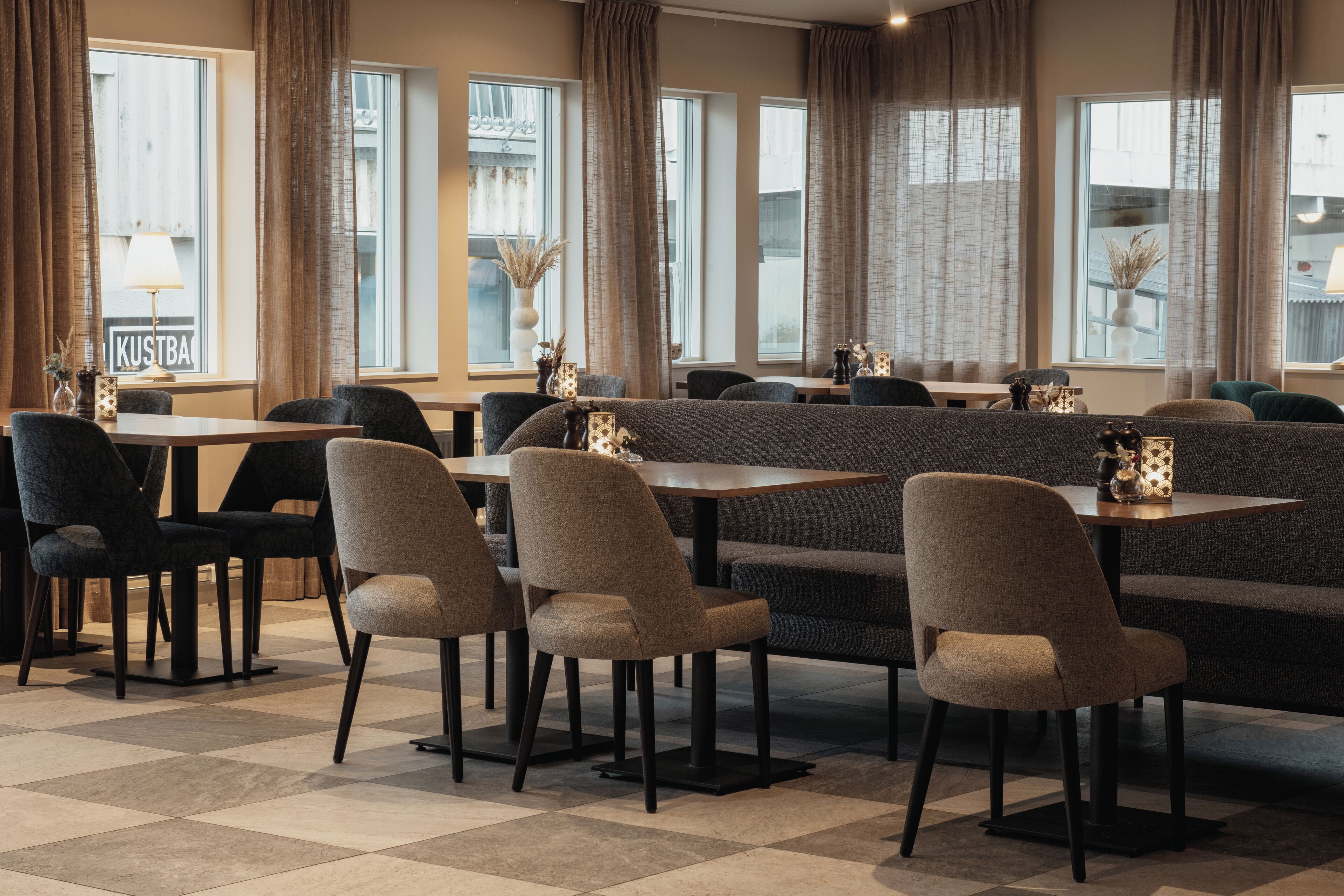 A modern dining area with a mix of tables and booths, large windows with curtains, and a checkered floor.