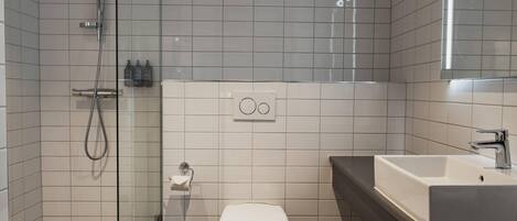 A modern bathroom with a glass shower enclosure, a white toilet, and a large sink with a mirror above it.