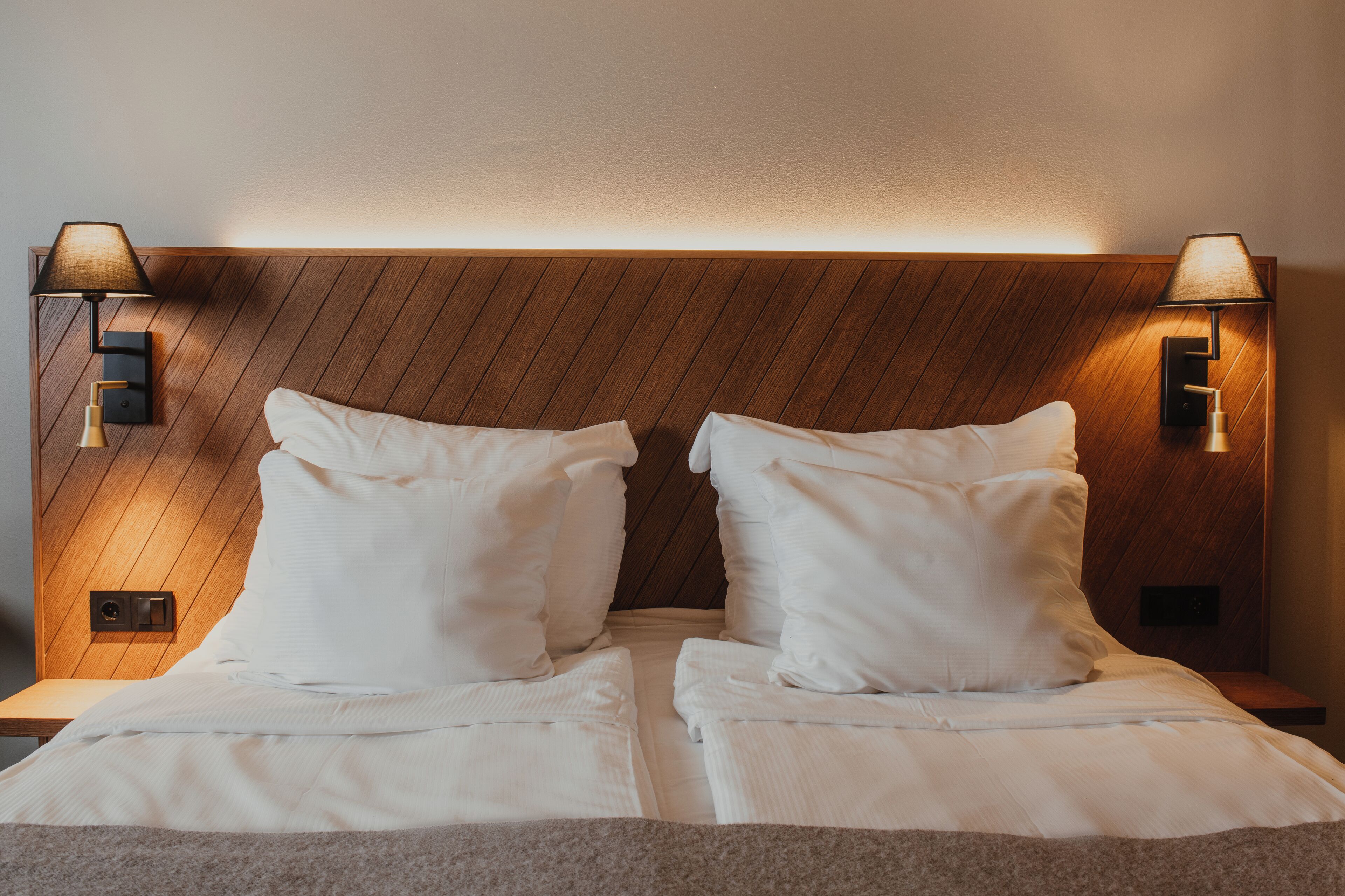 A double bed with white linens, two bedside lamps, and a wooden headboard.