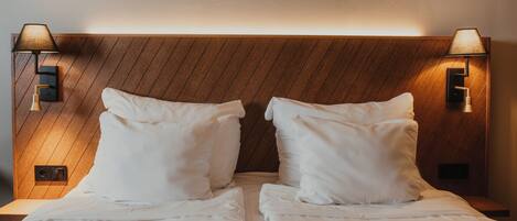 A double bed with white linens, two bedside lamps, and a wooden headboard.